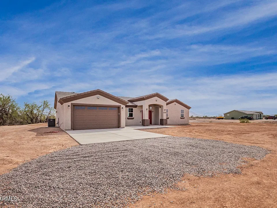 New stucco home with two-car garage, concrete driveway, and gravel site work