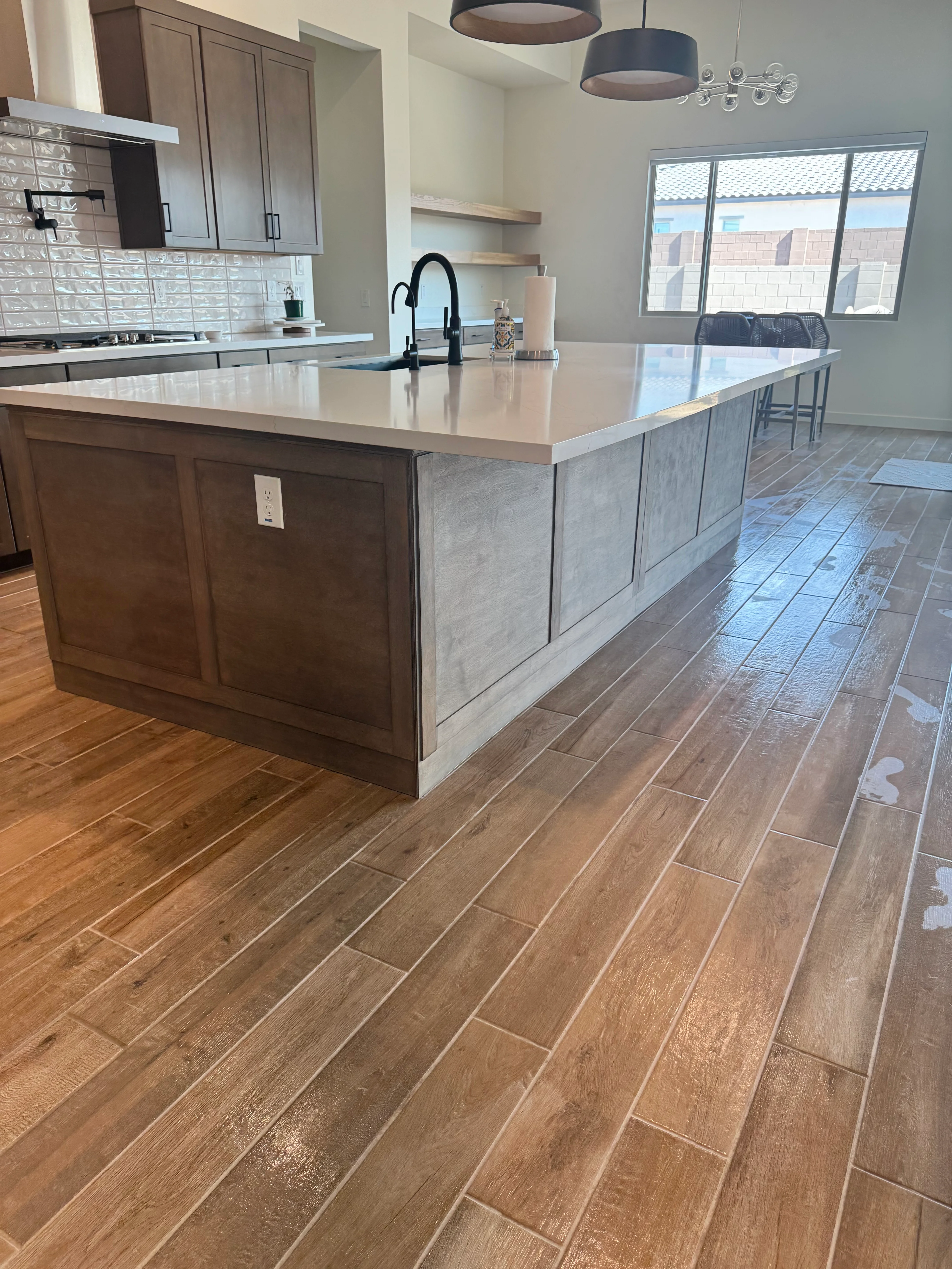 Modern kitchen with wood cabinetry, quartz island, herringbone tile flooring, and glass backsplash