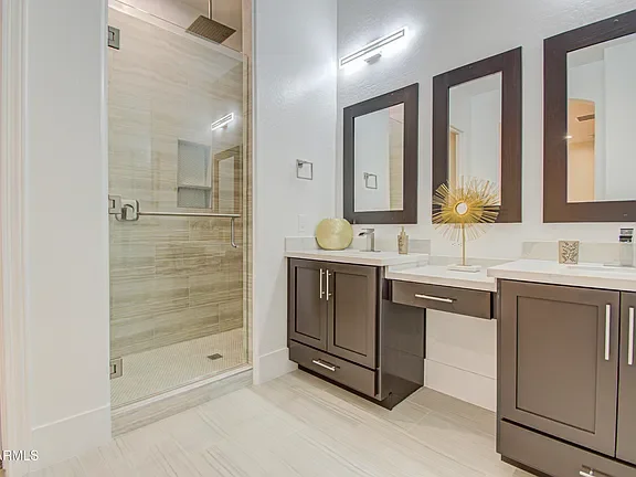 Modern bathroom with frameless shower, dual vanity, dark cabinets, and white tile flooring