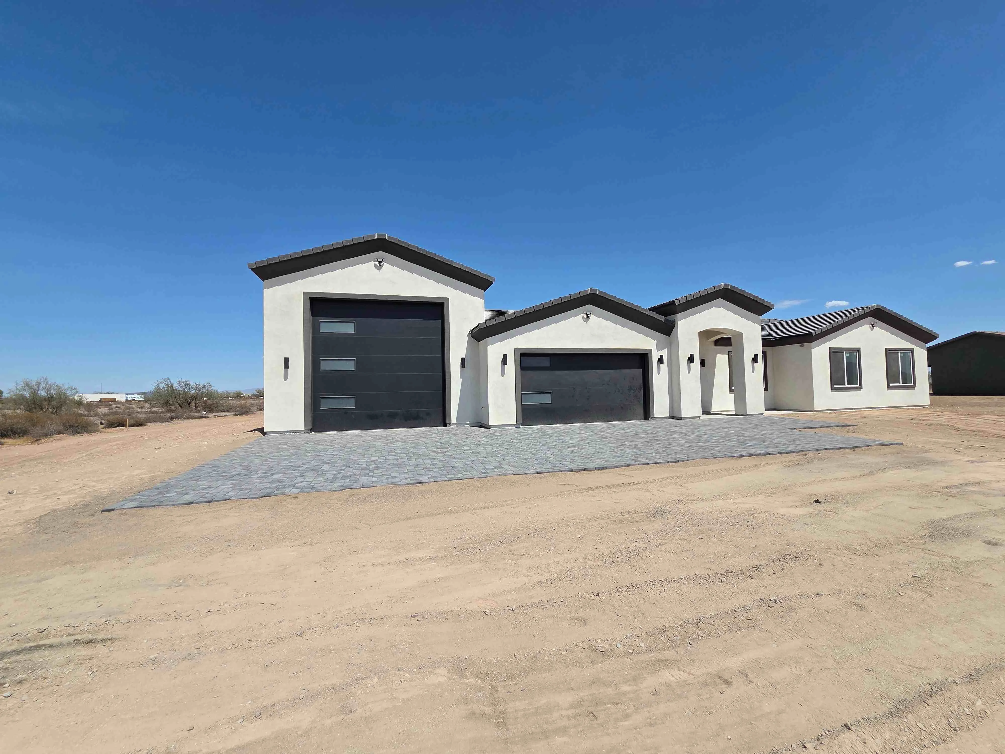 White stucco home with dark roof and two attached garage bays, paver driveway