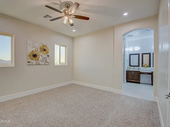 Master bedroom with carpet flooring, ceiling fan, and arched doorway to ensuite bathroom with dual vanities
