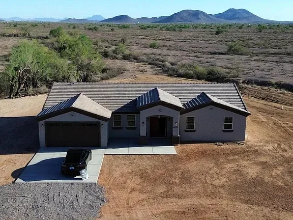 New construction home with white stucco exterior, metal roof, and two-car garage on prepared lot