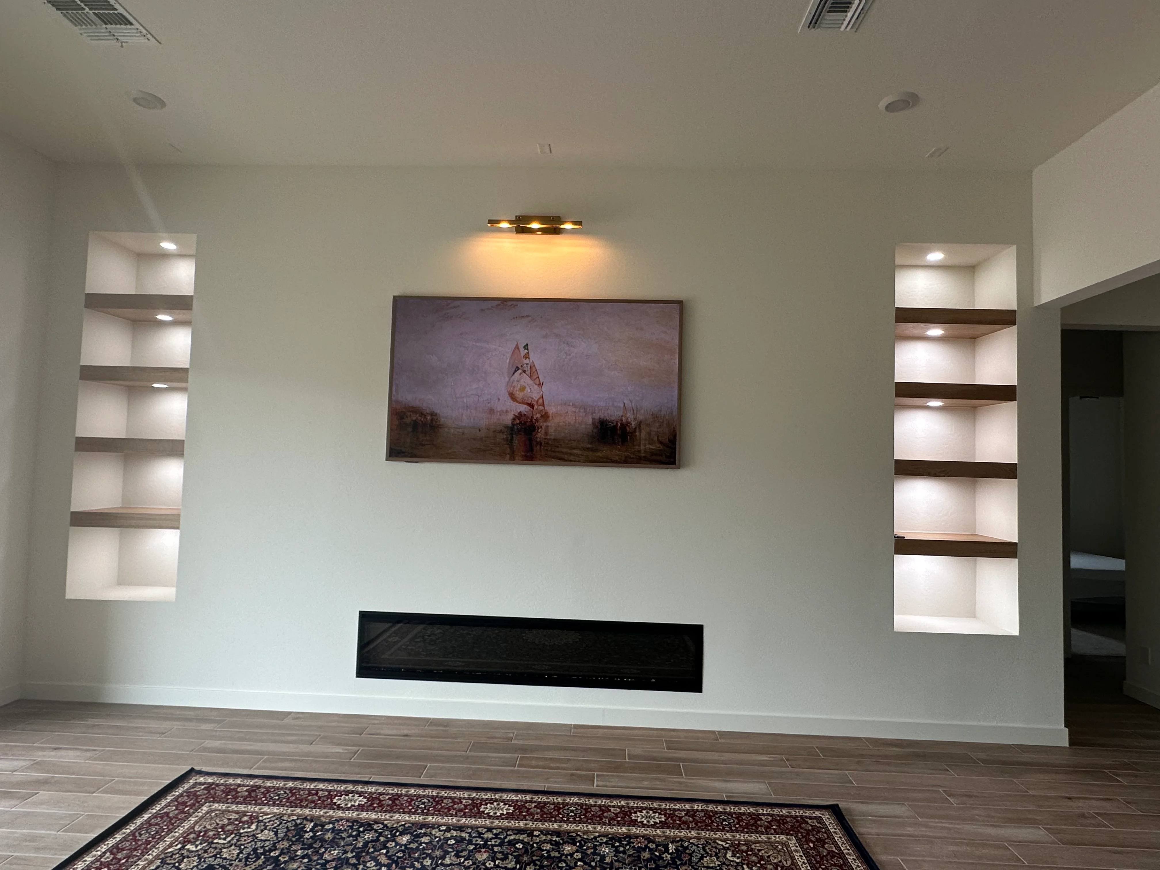Custom built-in shelving with LED lighting flanking black linear fireplace, white drywall, wood trim