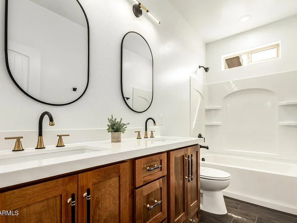 Master bathroom with wood vanity, white quartz counters, dual sinks, and tiled shower