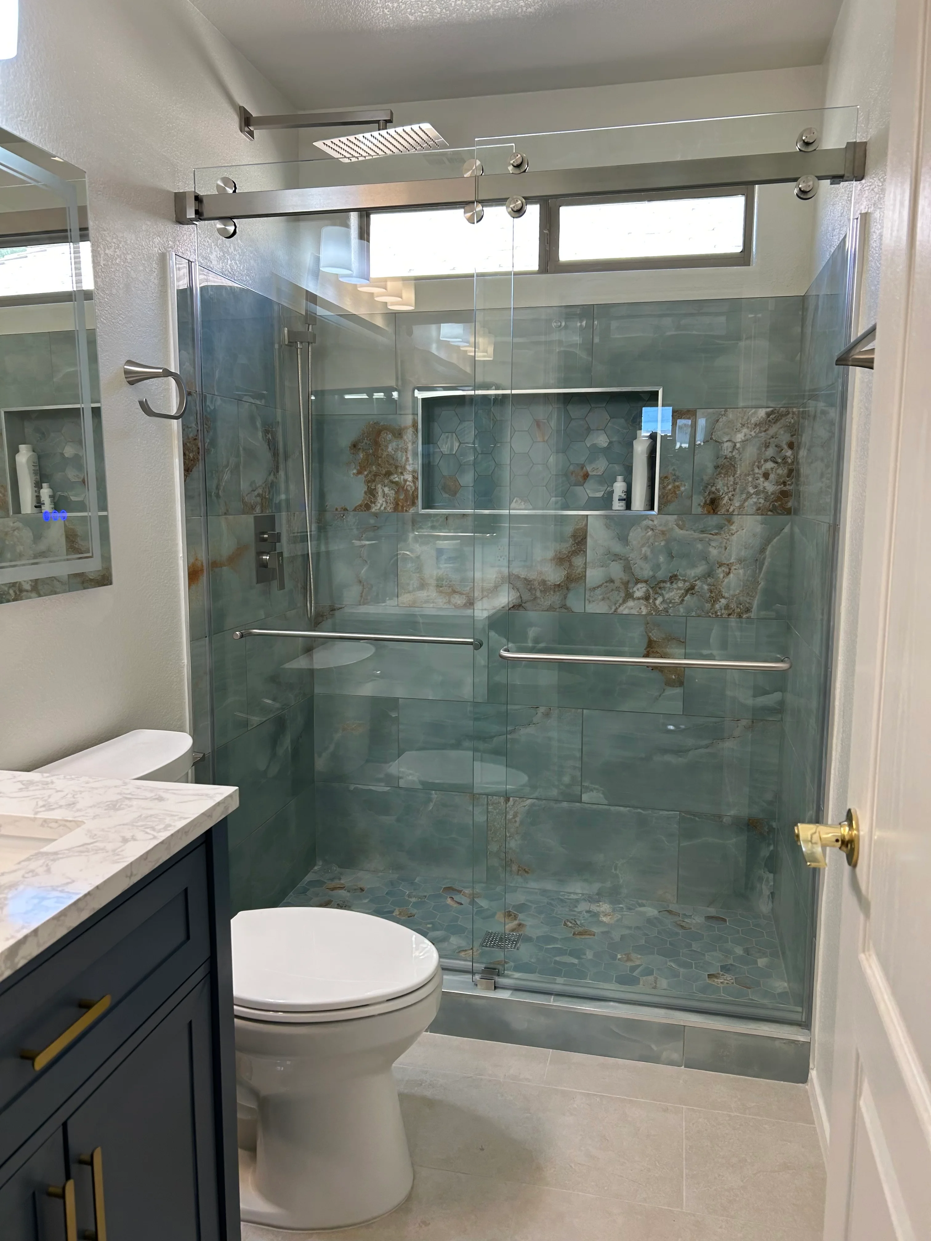 Frameless glass shower with green slate tile, marble vanity, and dark cabinetry
