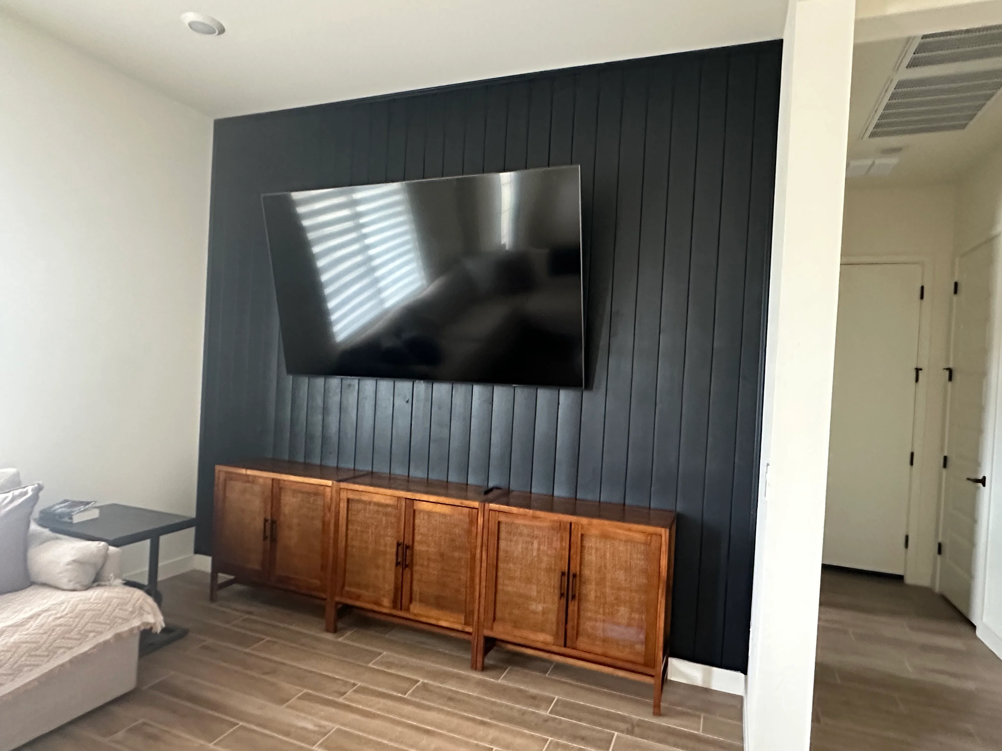 Dark shiplap accent wall with mounted TV and wood cabinet base in bedroom