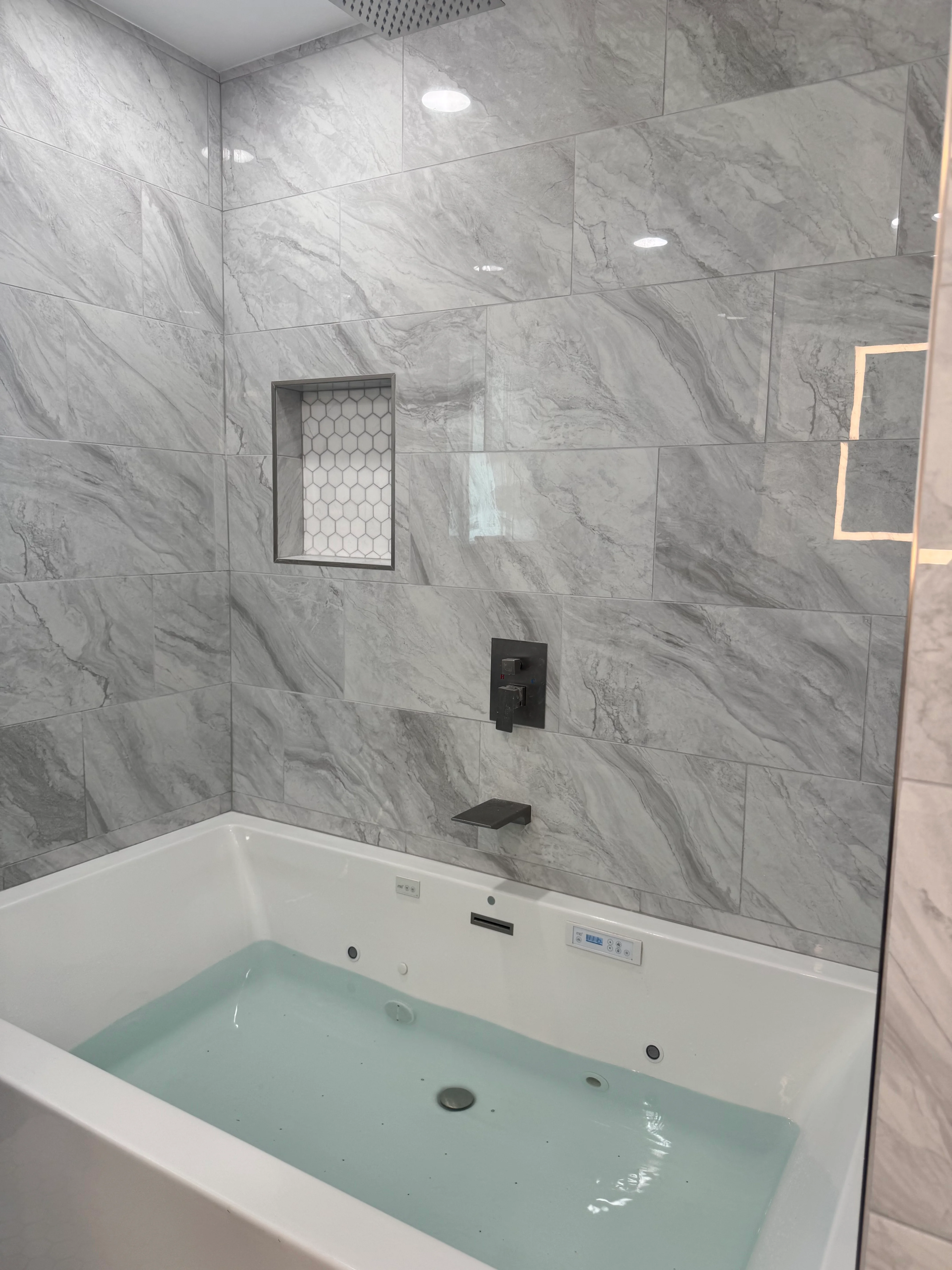 Marble tile shower with frameless glass door, black fixtures, and white soaking tub